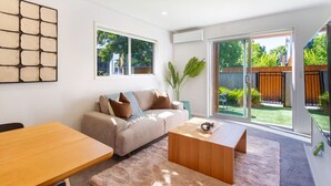 Una sala moderna con un sofá, una mesa de centro y una mesa de comedor. Una ventana grande ofrece vistas al exterior.