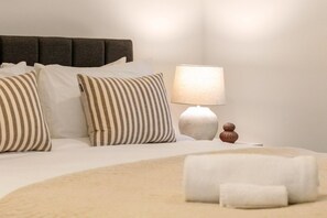 A neatly made bed with striped pillows, a bedside lamp, and a rolled towel on the floor. - Colombo St Retreat | Garage | Ideal For Long Stays (Christchurch)