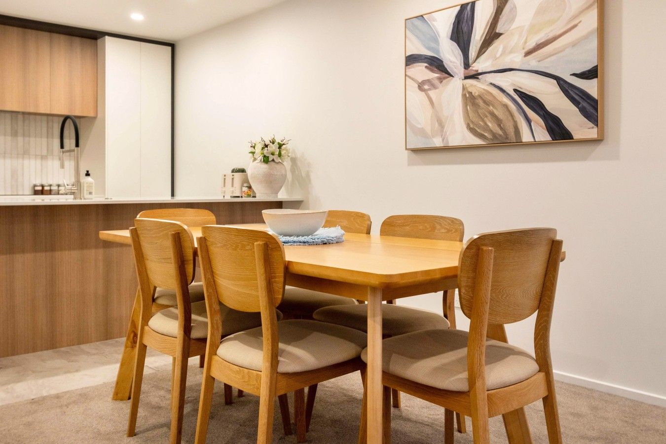 Un coin repas avec une table et des chaises en bois, un vase rempli de fleurs et un tableau accroché au mur.