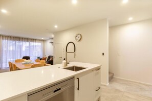 A modern kitchen with a white countertop, a built-in dishwasher, and a clock on the wall. - Colombo St Retreat | Garage | Ideal For Long Stays (Christchurch)