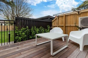 A wooden deck with a table and two chairs, surrounded by a black fence and greenery. - Colombo St Retreat | Garage | Ideal For Long Stays (Christchurch)