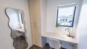 A modern bedroom with a desk, chair, wardrobe, and a window with a city view.