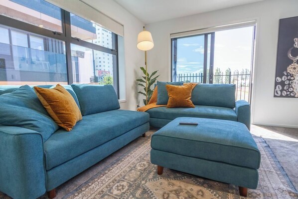 A living room with a teal sofa set, a matching ottoman, and a patterned rug.