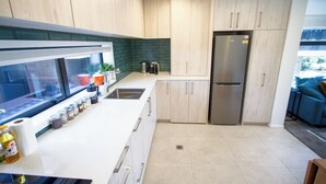 A modern kitchen with light wood cabinets, a stainless steel refrigerator, and a window overlooking a green outdoor area.
