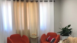 Un salon moderne avec deux fauteuils rouges, une petite table d’appoint avec des bougies, un canapé blanc et un grand tapis blanc.