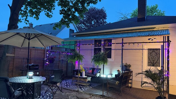 Un espace patio avec une table ronde, des chaises, un pot de fleurs et des guirlandes lumineuses.