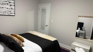 Une chambre à coucher comprenant un lit, une table de chevet, un miroir, une porte et une œuvre d’art accrochée au mur.
