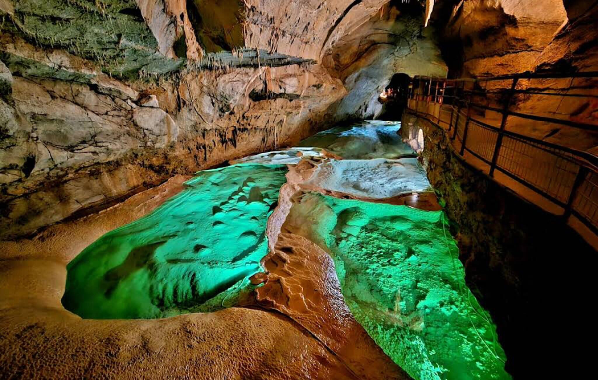 Eine Höhle mit einem Wasserbecken, das grünes Licht reflektiert, umgeben von felsigen Wänden.