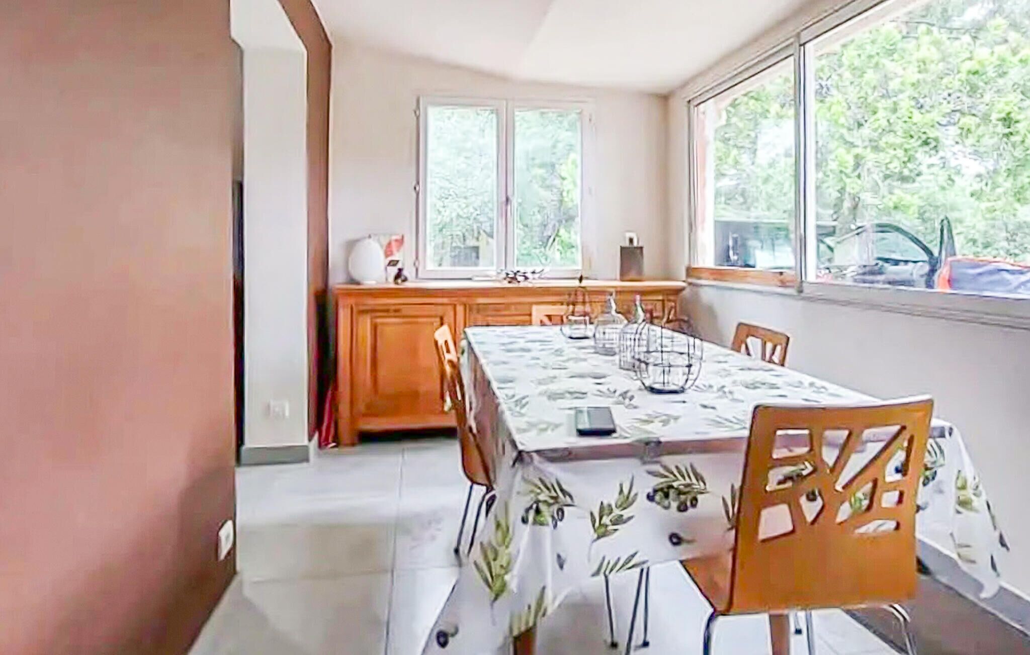 A dining area with a table set for four, a wooden cabinet, and a window with a view of greenery.