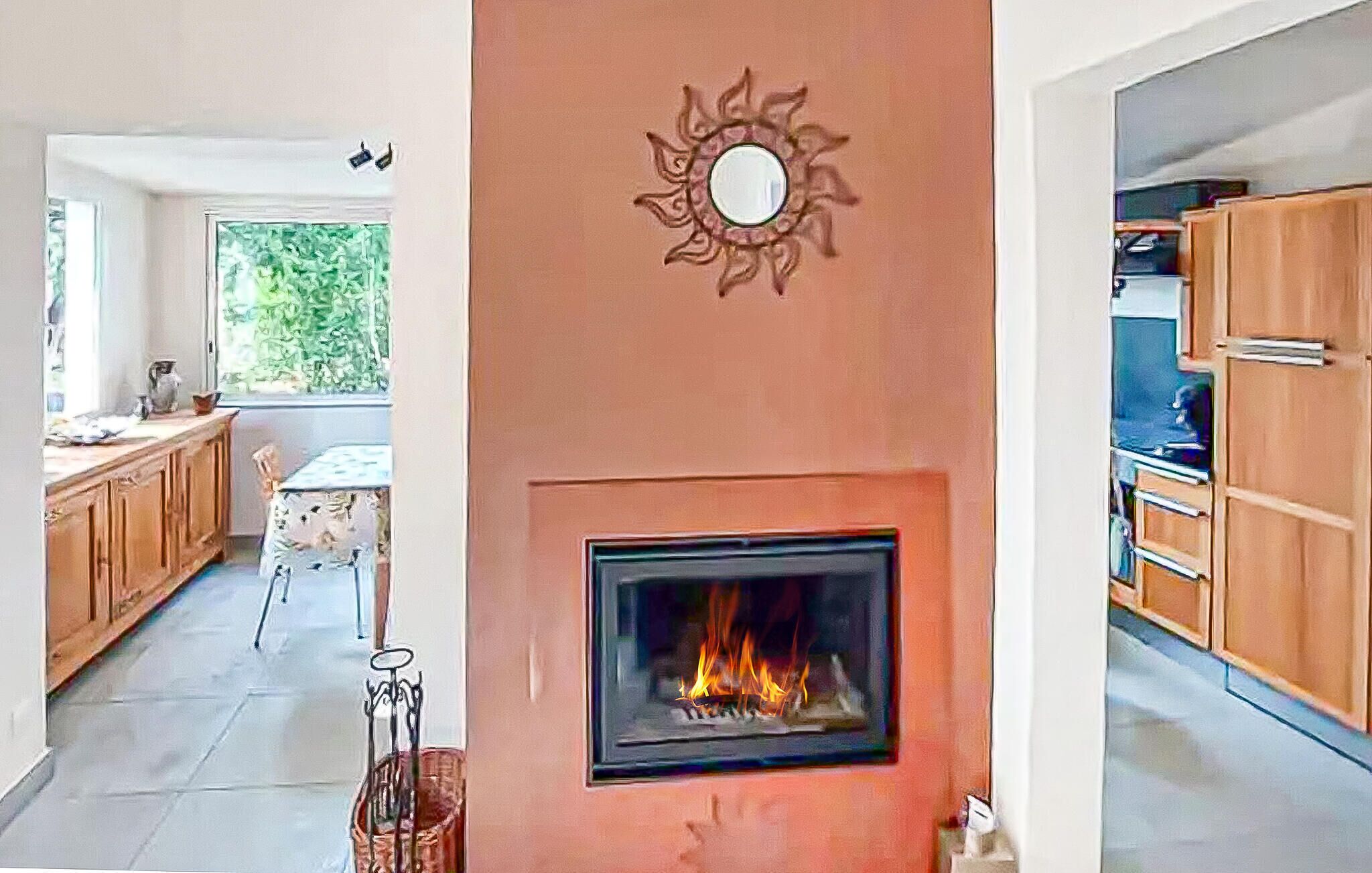 Eine moderne Küche mit Kamin, Holzschränken und einem Essbereich mit Blick ins Grüne.