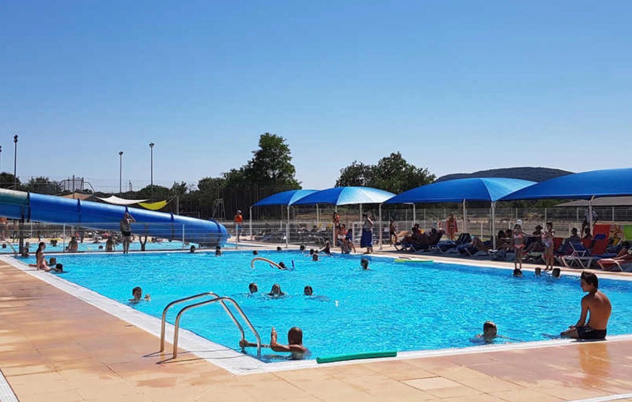 Una piscina con tobogán acuático, tumbonas y sombrillas.