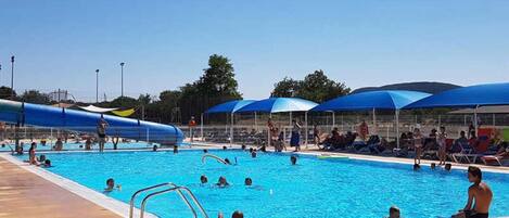 Una piscina con tobogán acuático, tumbonas y sombrillas.