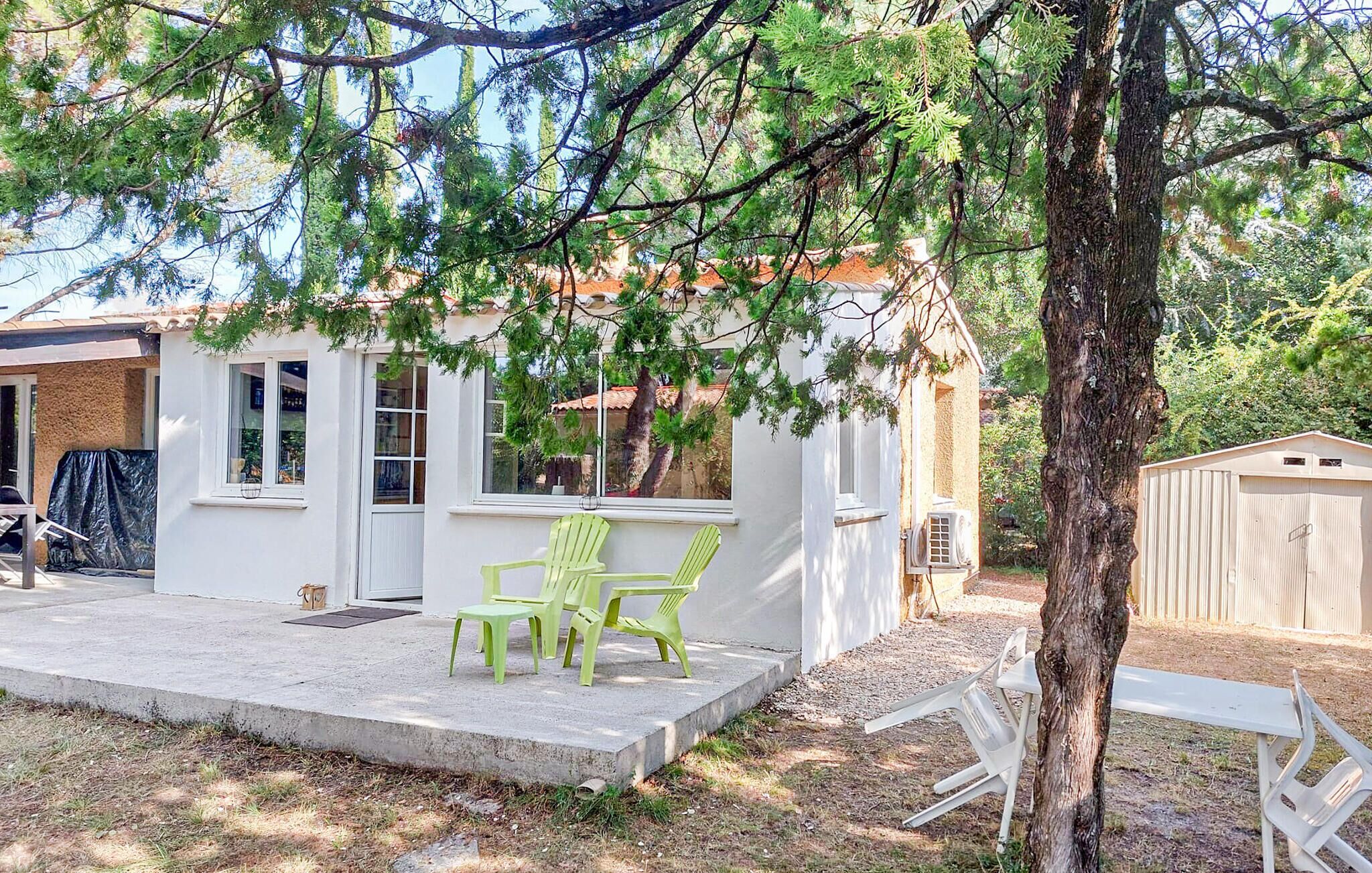 A small white house with a porch, two green chairs, and a tree in the foreground.