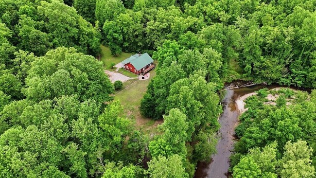 A red house surrounded by dense green forest and a small stream.