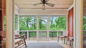 A spacious balcony with a wooden deck, a ceiling fan, and a view of a forested area.