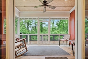 Ein geräumiger Balkon mit Holzboden, Deckenventilator und Blick auf eine bewaldete Gegend.