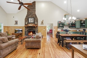 A spacious living room with a fireplace, wooden flooring, and a dining area with a chandelier.