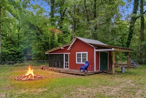A red cabin with a fire pit, a chair, and a door.