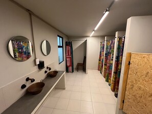 Ein modernes Badezimmer mit einem langen Waschtisch, zwei Waschbecken, einem Spiegel und einer Duschkabine mit bunten Vorhängen.