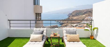 A balcony with two sun loungers, a small table with fruit and wine glasses, and a potted plant.