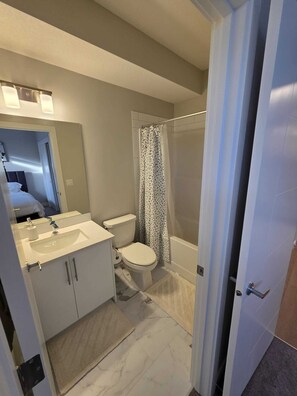 A modern bathroom with a white sink, toilet, and shower area. - Cheerful Home away from Home (Calgary)