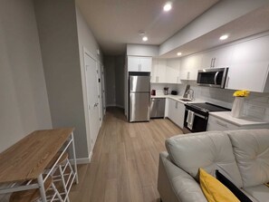 A modern kitchen with white cabinets, stainless steel appliances, and a wooden dining table. - Cheerful Home away from Home (Calgary)