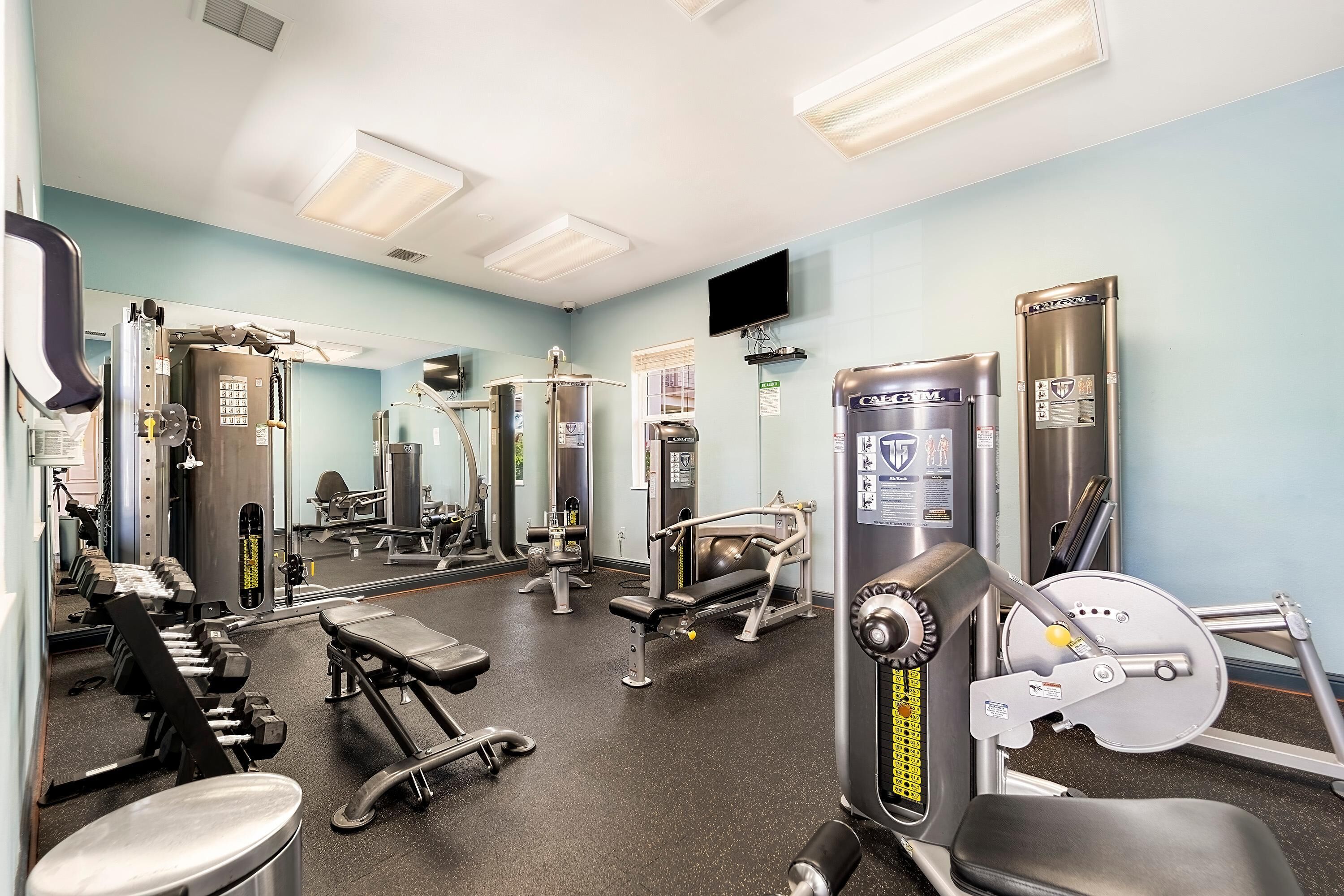 A gym with various exercise equipment, including dumbbells, benches, and weight machines.