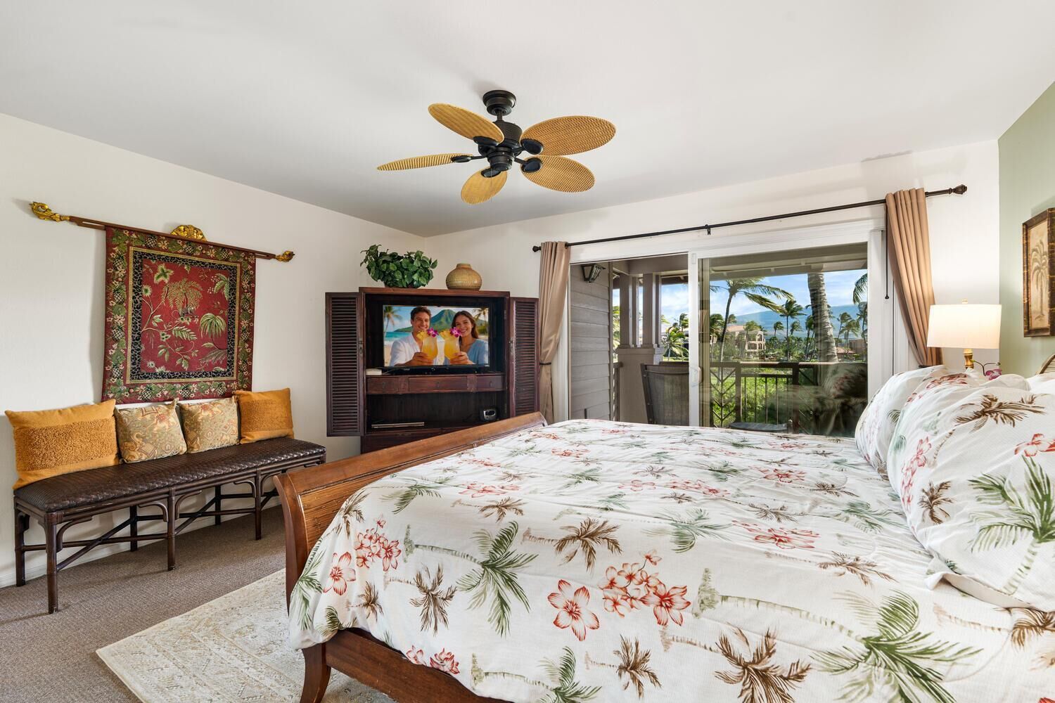 A hotel room with a bed, a bench, a TV, a ceiling fan, and a balcony with a view.