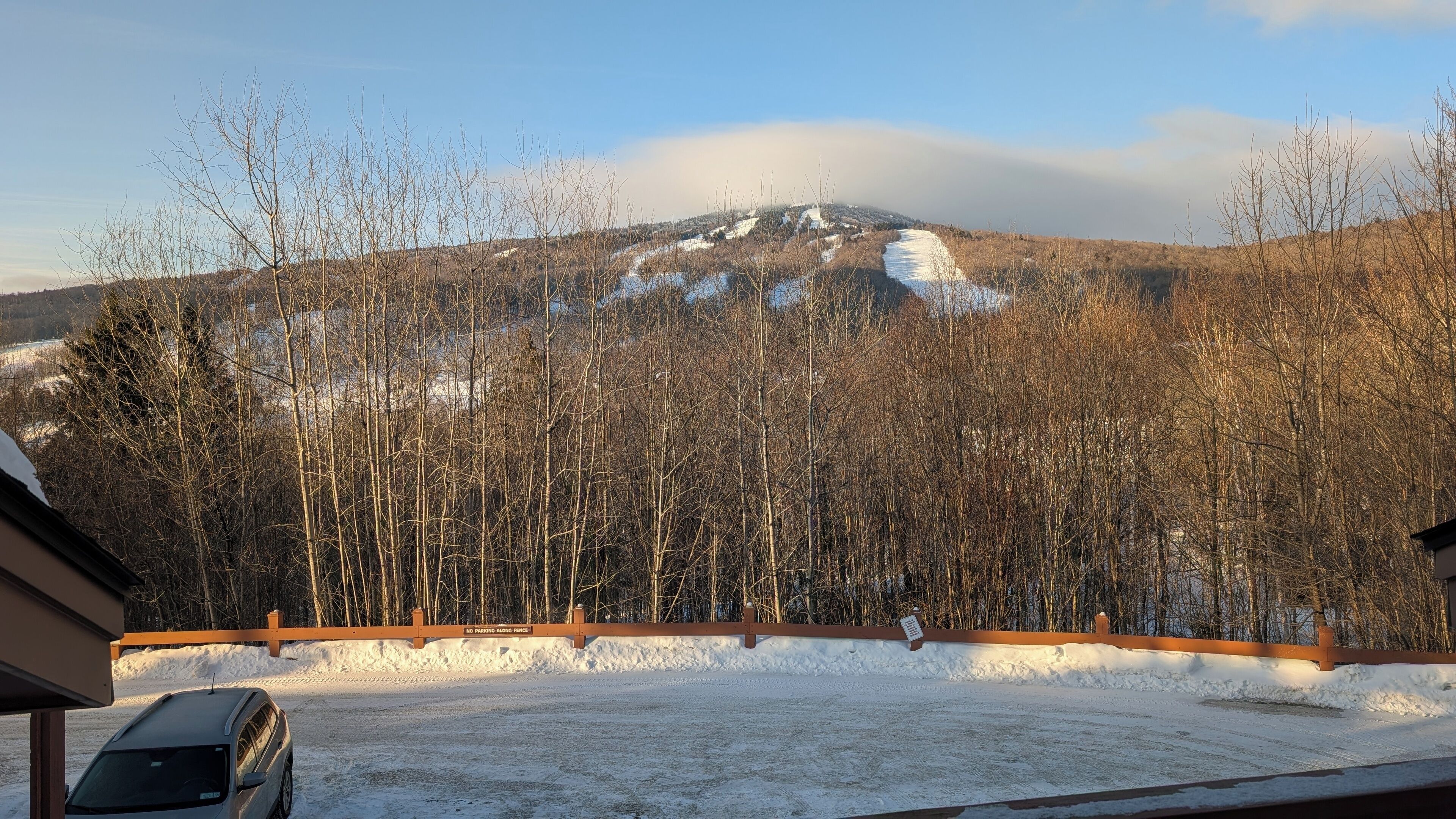 Un paysage enneigé avec une montagne en arrière-plan, un ciel dégagé et une voiture garée dans une allée.