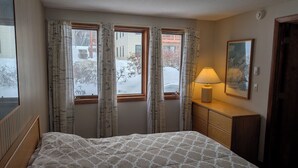 Ein Schlafzimmer mit einem Bett, einem Nachttisch mit Lampe und einem Fenster mit Vorhängen.