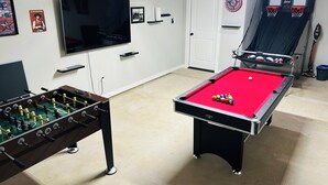 Une pièce équipée d’une table de billard, d’un baby-foot, d’une télévision et d’un panier de basket.
