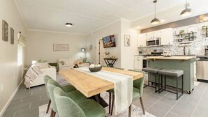 A modern kitchen with white cabinets, a central island, and a dining area with a wooden table and green chairs. - Luxurious One-Bedroom Gem Near Conneaut Lake (Conneaut Lakeshore)
