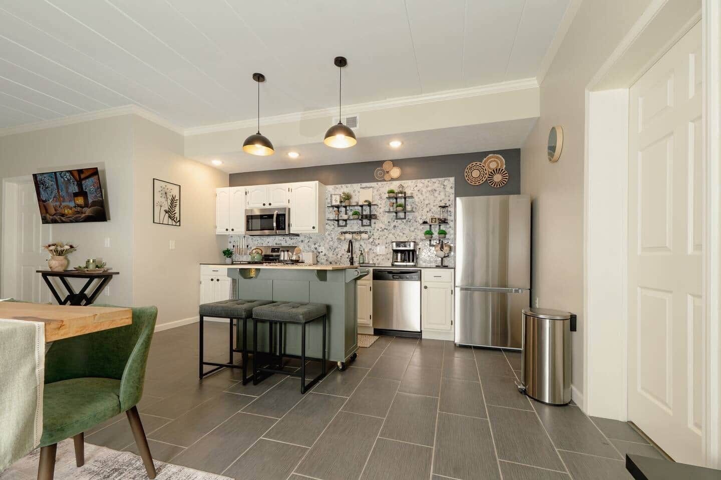 Una cocina moderna con una isla central, iluminación colgante y un refrigerador de acero inoxidable.