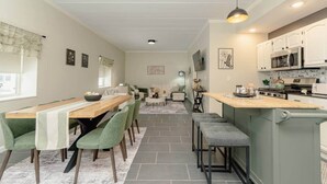 A modern kitchen with white cabinets, a wooden island, and a dining area with green chairs and a wooden table. - Luxurious One-Bedroom Gem Near Conneaut Lake (Conneaut Lakeshore)