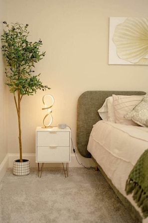 A bedroom with a bed, bedside table, lamp, and a potted plant.