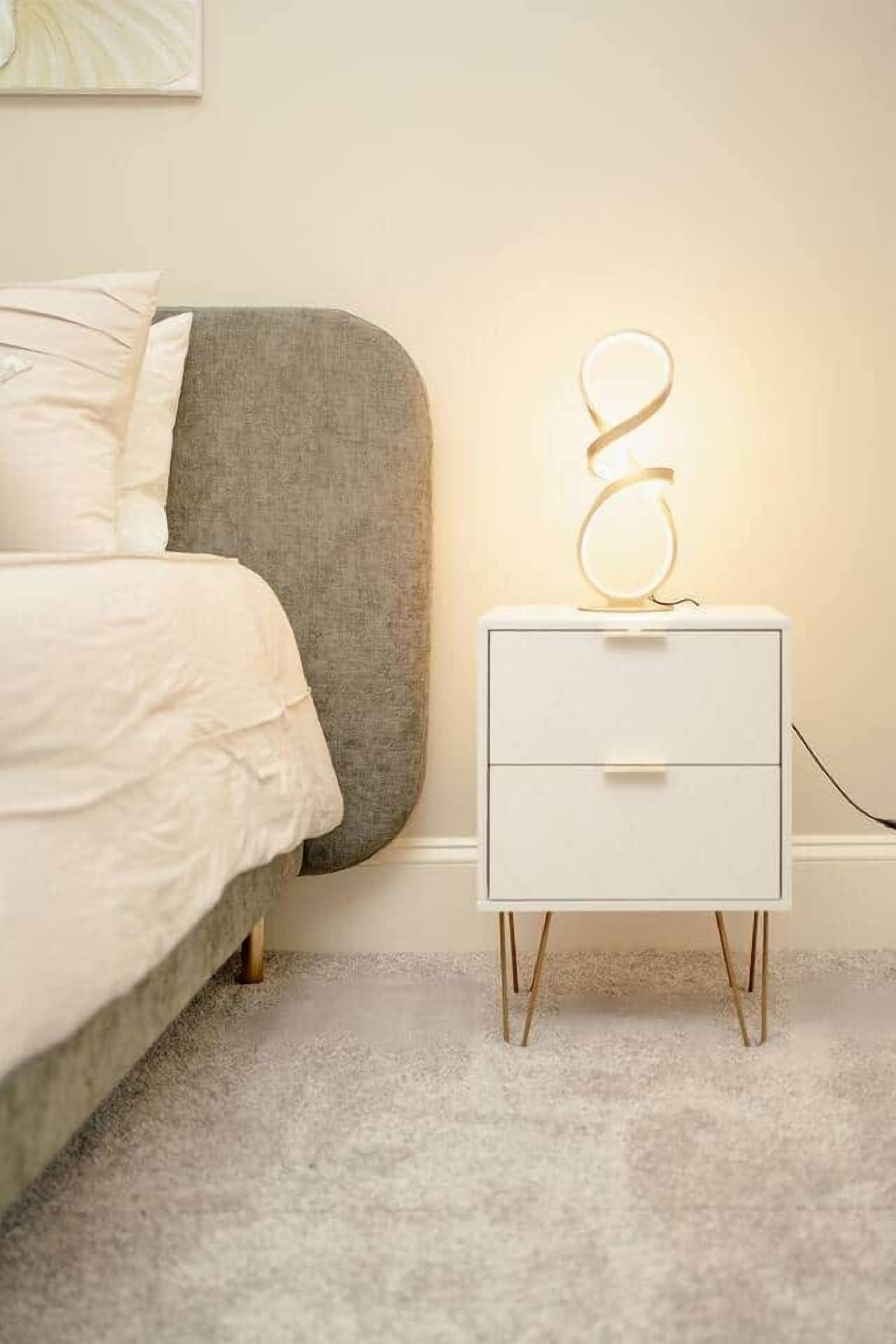 Quarto com cama, mesa de cabeceira com abajur e obra de arte na parede.