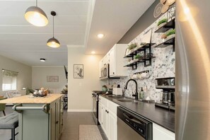 Une cuisine moderne dotée d’un îlot central, d’appareils électroménagers en acier inoxydable et de luminaires suspendus.
