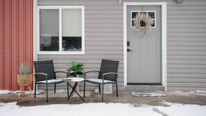 A house with a gray exterior, a red siding section, a front door with a wreath, and two chairs and a table outside. - Luxurious One-Bedroom Gem Near Conneaut Lake (Conneaut Lakeshore)