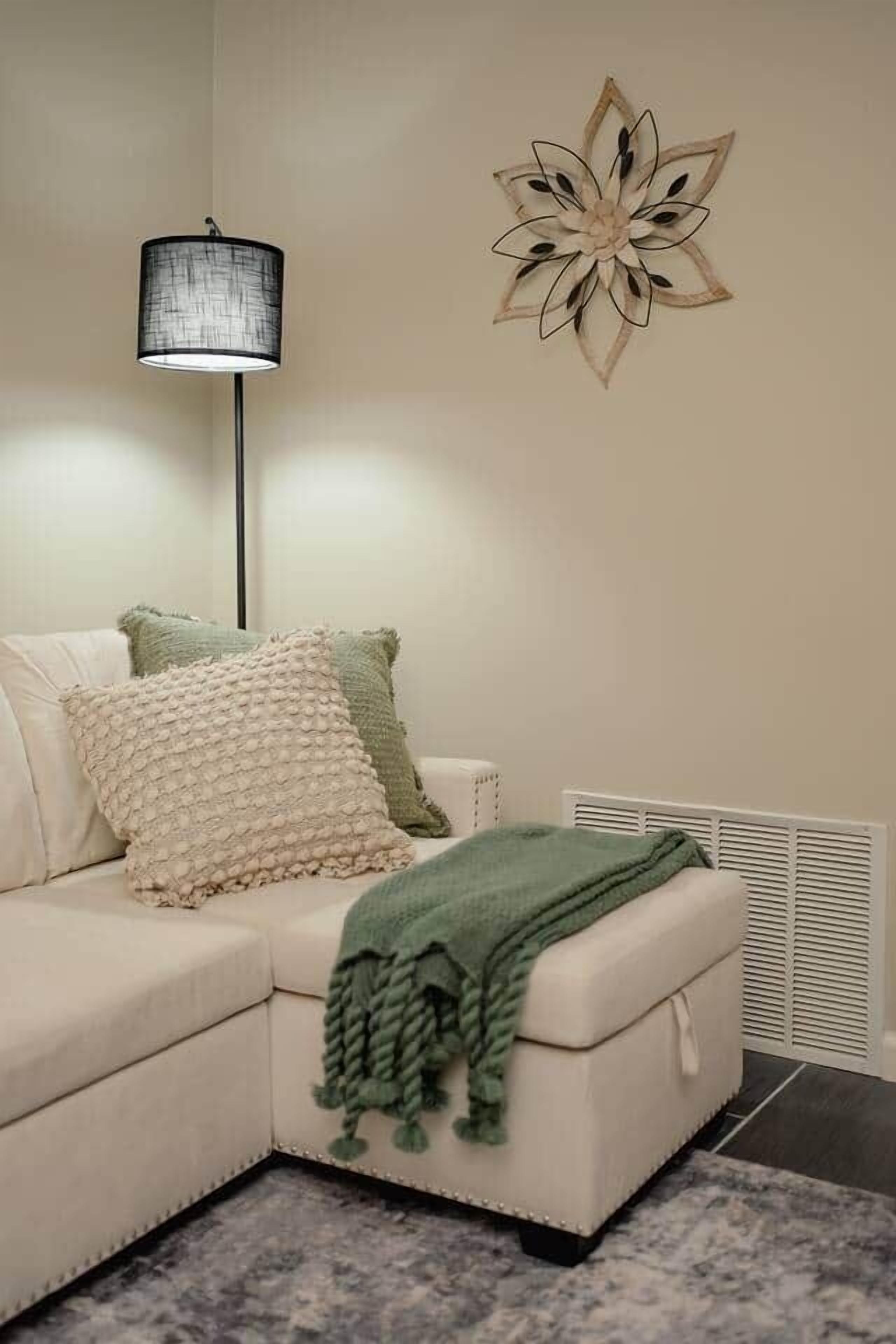 A modern living room with a sectional sofa, a floor lamp, a decorative wall piece, and a green throw blanket.