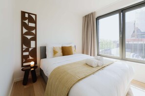 Una camera d'albergo con un letto, un comodino, un'opera d'arte a parete e una finestra con tende.