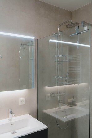 Un bagno moderno con doccia vetrata, lavabo bianco e specchio grande.
