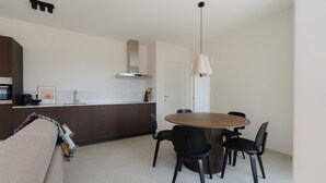 Une cuisine moderne avec des meubles en bois foncé, un plan de travail blanc et une hotte en acier inoxydable. On y trouve également un coin repas avec une table ronde en bois et des chaises noires.