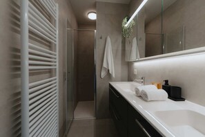 Een moderne badkamer met een douchecabine van glas, een wit wastafelmeubel met een grote spiegel en een handdoekhouder.