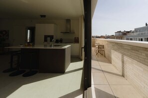 Een moderne keuken met een centraal eiland, een eethoek met stoelen en een uitzicht op de stad vanaf een balkon.