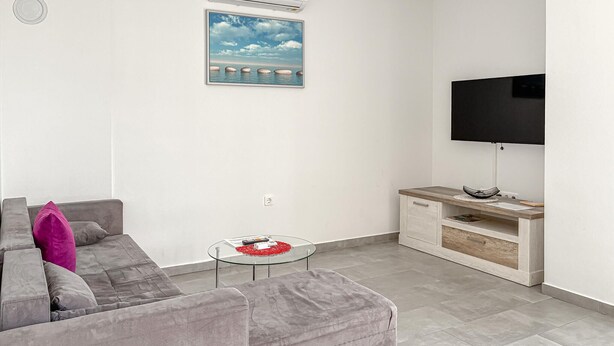 Ein modernes Wohnzimmer mit grauem Sofa, einem Glastisch, einem Flachbildfernseher und einem Holz-TV-Schrank.