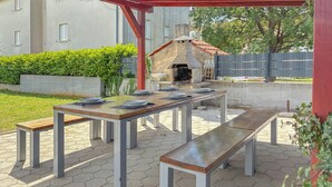 Eine Terrasse im Freien mit einem Stein-Barbecue, einem Holztisch gedeckt mit Tellern und Bänken.