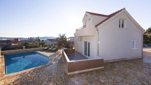 Una casa de dos pisos amb piscina, paviment de pedra i vista a la ciutat al fons.