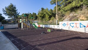 Un parc infantil amb estructures per escalar i tobogan, envoltat d'una zona pavimentada i un mur amb grafitis.