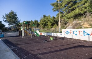 A playground with climbing structures and a slide, surrounded by a paved area and a wall with graffiti. - Amazing home in Kastel Sucurac (Kastel Sucurac)