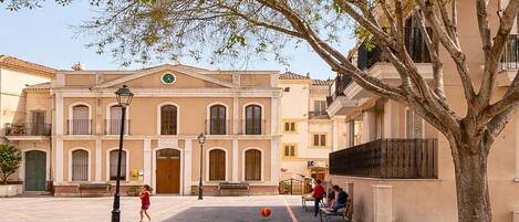 Un patio con un edificio que tiene una entrada principal, un árbol y una cancha de baloncesto.